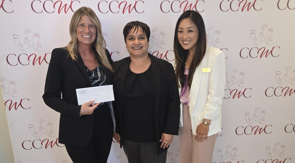 Three women stand in front of a backdrop with the CCWC logo for presentation of a grant to help support the Tech Bridge project.