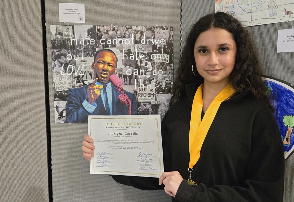 A girl student stands beside her winning artwork at a student art competition.