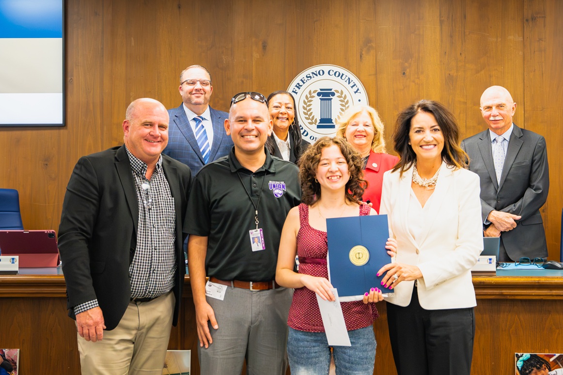 Fresno County Superintendent of Schools staff and representatives gather with a student during a Board of Education recognition as the Superintendent's Superstar, celebrating her accomplishments and presenting her with a certificate of recognition.