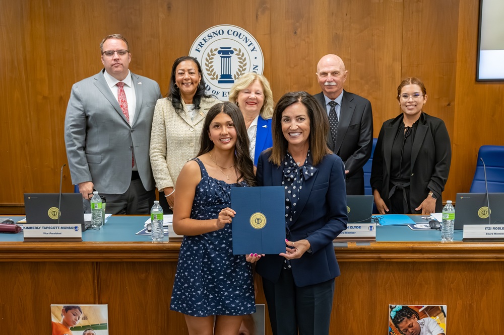 Student standing with her award certificate and the Superintendent of Schools with the board of education behind them.