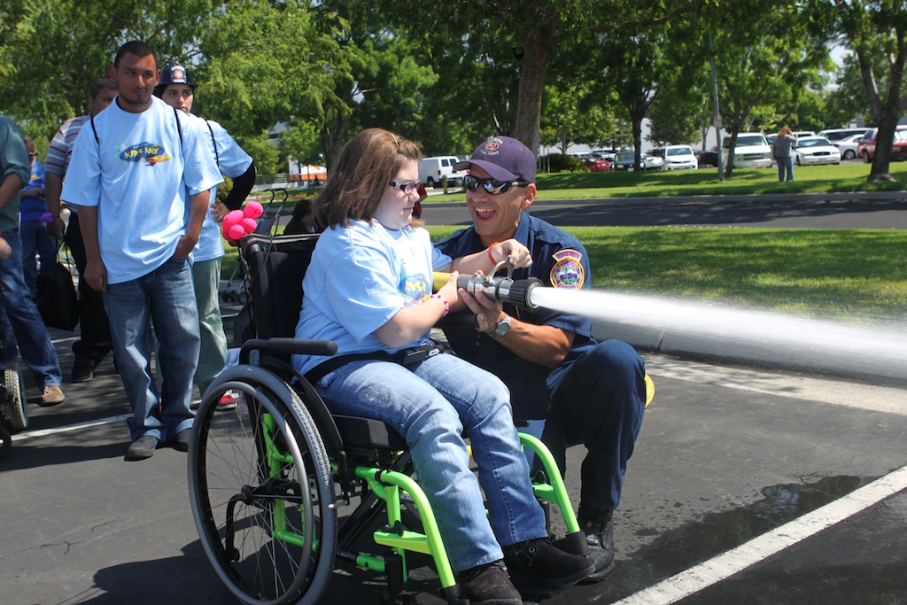 kid in wheelchair using fire hose with the help of firefighter